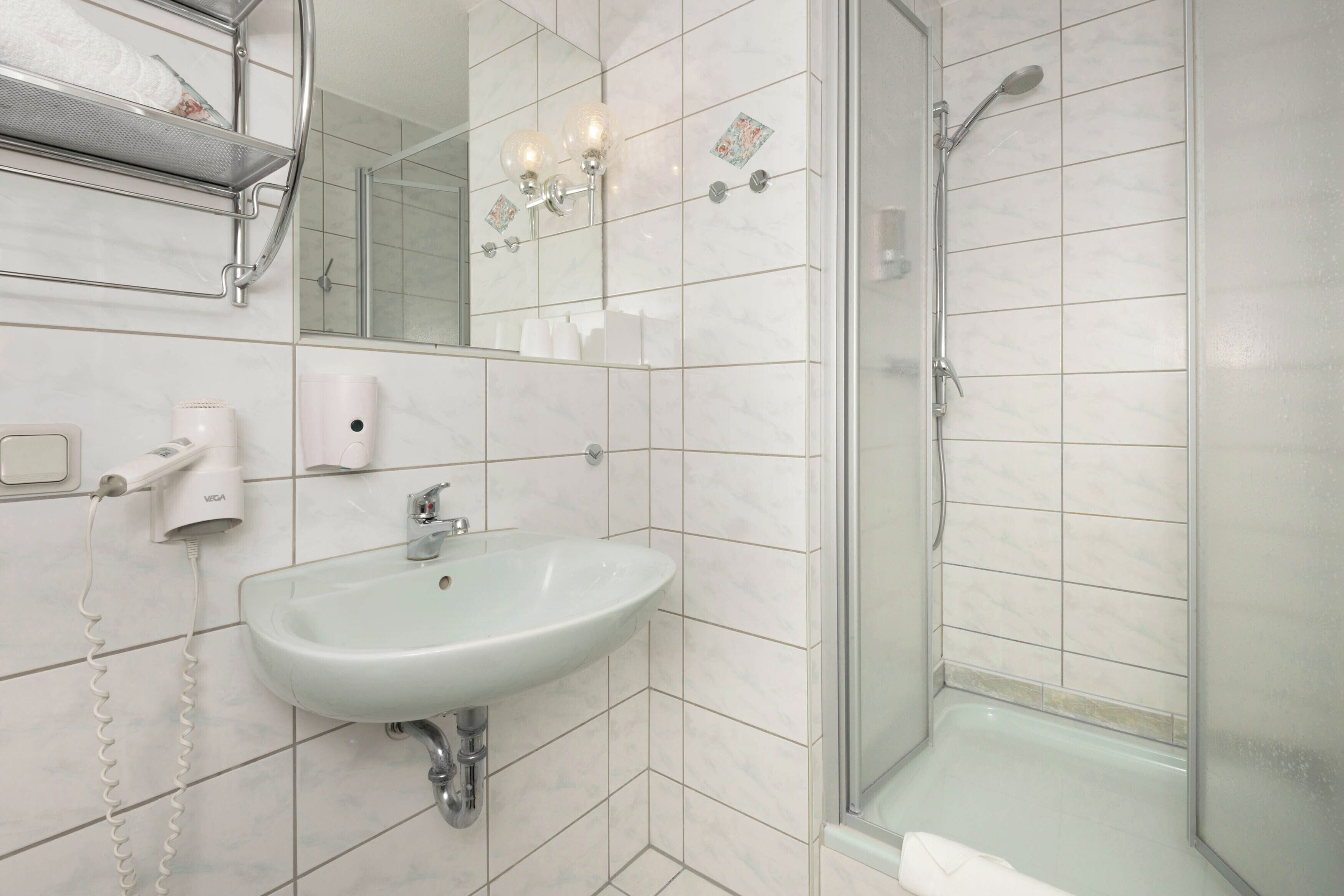 Ein Badezimmer mit Waschbecken, Spiegel, Dusche und Handtuchhalter.