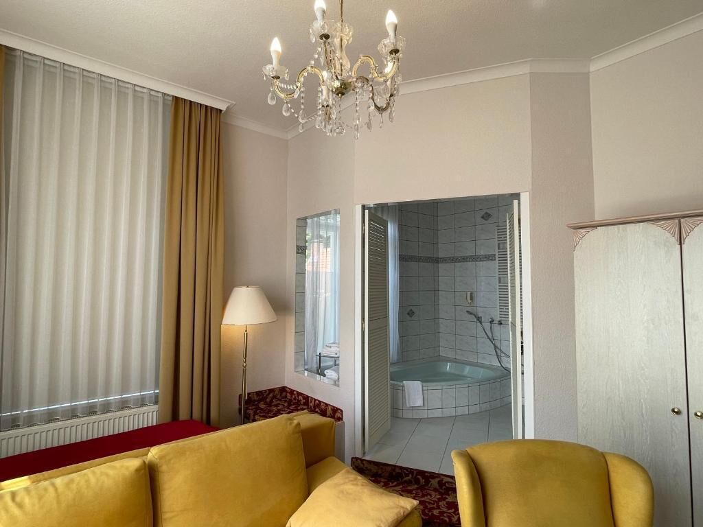 Une chambre d’hôtel avec un canapé jaune, un lustre, une douche séparée par des parois de verre et une armoire.