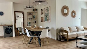 A modern living room with a dining area, a sofa, a coffee table, and a washing machine in the background. - La Cabine de Jeanne - 3 rooms close to beach, port, restaurants on foot (Saint-Gilles-Croix-de-Vie)