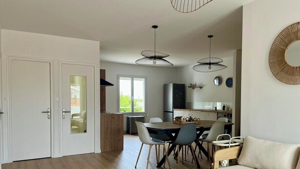 A modern living room with a sofa, dining table, and chairs. There is a kitchen area with a refrigerator and a window. - La Cabine de Jeanne - 3 rooms close to beach, port, restaurants on foot (Saint-Gilles-Croix-de-Vie)