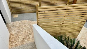 A wooden fence with horizontal slats, a brick pathway, and a white wall. - La Cabine de Jeanne - 3 rooms close to beach, port, restaurants on foot (Saint-Gilles-Croix-de-Vie)