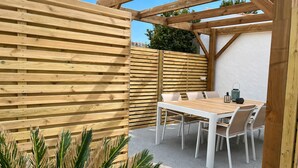 A wooden pergola structure with a table and chairs, surrounded by a wooden fence and a white wall. - La Cabine de Jeanne - 3 rooms close to beach, port, restaurants on foot (Saint-Gilles-Croix-de-Vie)