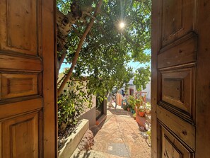 An open wooden door leading to a narrow alley with a tree branch overhanging, potted plants, and a clear sky. - Casa de Santa Catarina - Unique Authentic Charm (Faro)