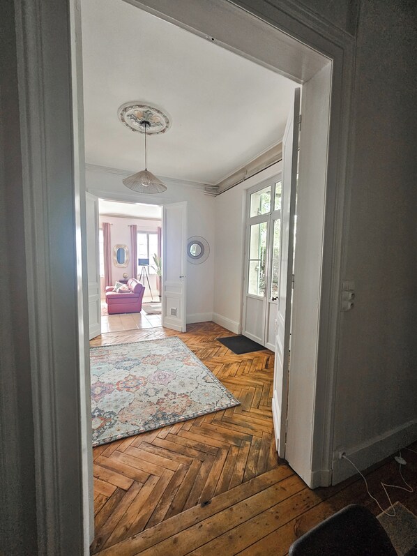 Un pasillo con suelo de madera, un tapete estampado, un ventilador de techo y una puerta que da a otra habitación.