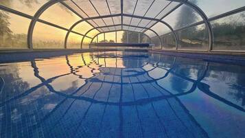 Une piscine intérieure dotée d’un toit incurvé et de murs en verre transparent.
