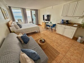Una habitación con cama, sofá, una mesita con una taza, televisión, zona de cocina y vistas al mar.