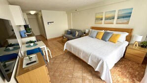 Habitación de hotel con cama, escritorio con silla, una mesita con planta y vistas a la playa a través de la ventana.