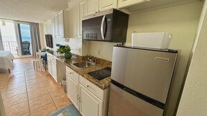 Una cocina con armarios blancos, un refrigerador de acero inoxidable, un microondas y un lavabo.