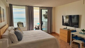 Habitación de hotel con cama, escritorio, televisor y balcón con vista al mar.