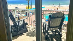 Un balcón con dos sillas Adirondack, una piscina y vistas a la playa y el océano.