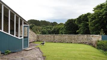 A stone wall, a grassy yard, and a building with a window.