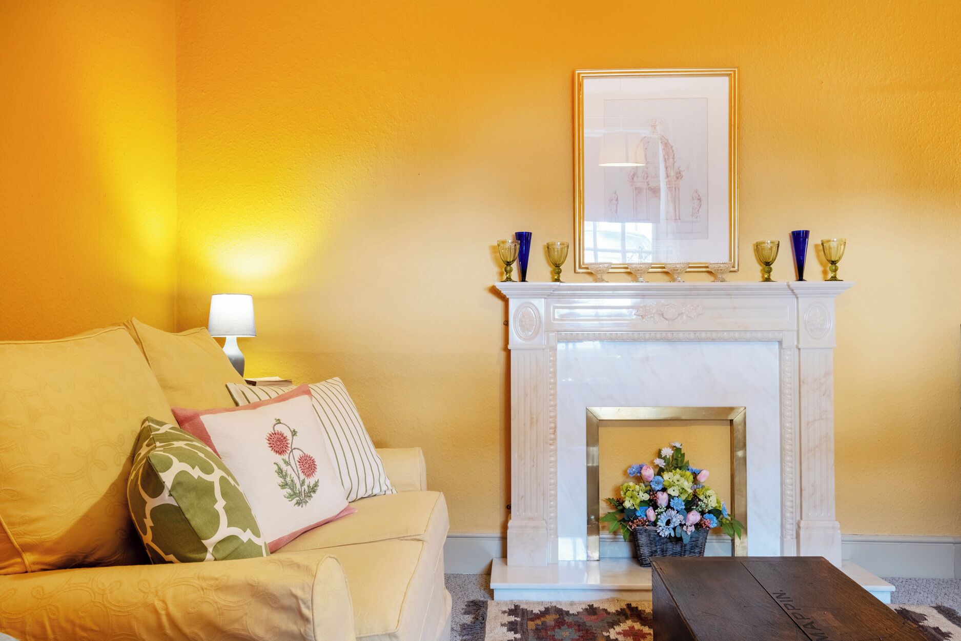 A living room with a sofa, a fireplace, a lamp, and a framed picture above the mantel.