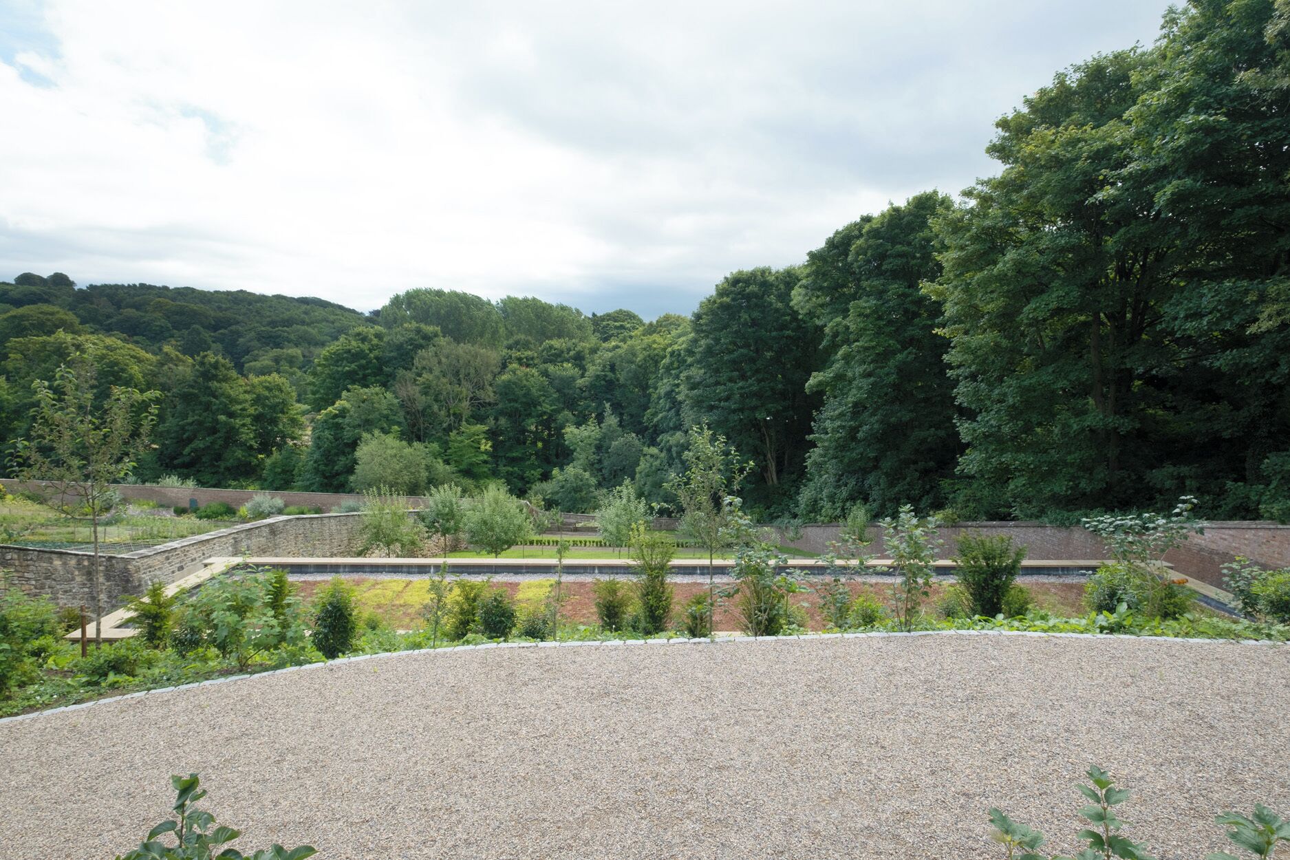 A gravel area with a stone wall and trees in the background.