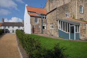 A stone building with a red-tiled roof, a fenced driveway, and a grassy yard. - Palace Garden Cottage (Bishop Auckland)