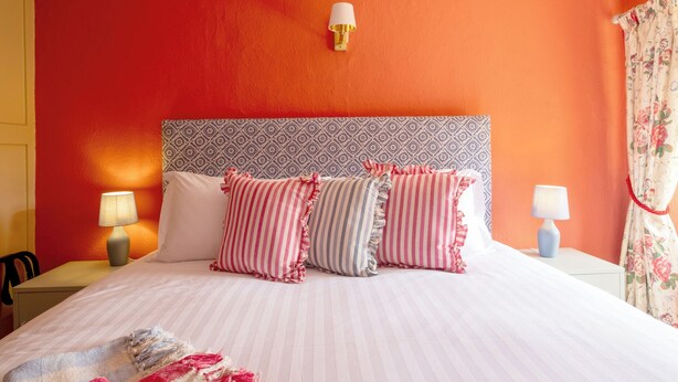 Una cama con almohadas a rayas, un cabecero estampado y dos lámparas de noche.