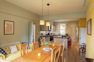 Una cocina amplia con electrodomésticos modernos, un comedor con mesa y sillas de madera, y una sala de estar acogedora con sofá y cojines.