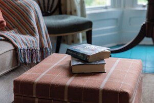 Una habitación con un reposapiés de cuadros, una manta a rayas y un libro sobre el reposapiés.