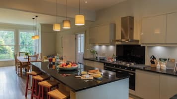 A modern kitchen with a large island, wooden bar stools, pendant lighting, and a view of the outdoors.