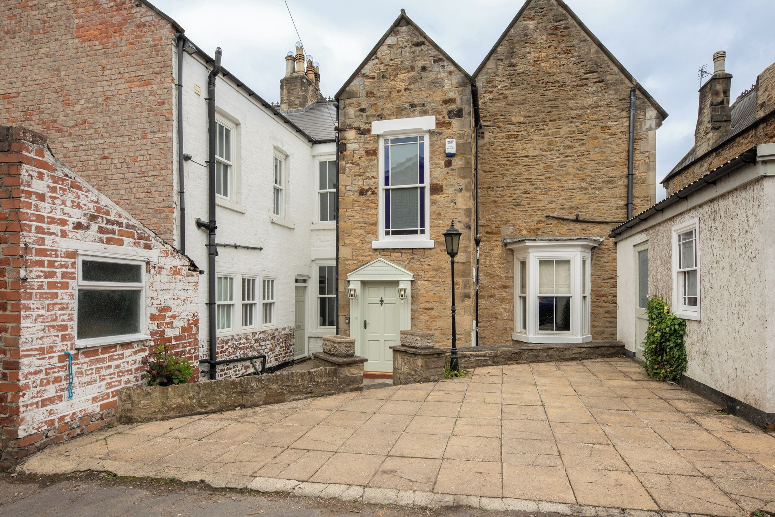 A courtyard with stone paving, a white door, and a stone building with a pitched roof.