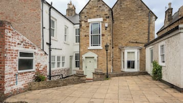 A courtyard with stone paving, a white door, and a stone building with a pitched roof.