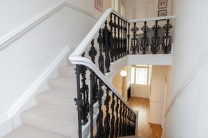 Una escalera con barandillas negras ornamentadas y peldaños cubiertos de alfombra beige.