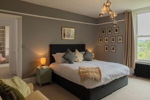 Un dormitorio con una cama grande, mesitas de noche, un cuadro en la pared y una ventana con cortinas.