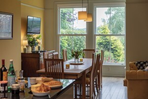 Comedor con mesa de madera, sillas y vistas a la vegetación a través de amplias ventanas.