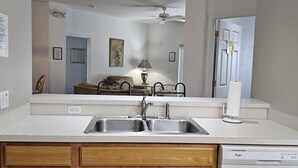 Une cuisine équipée d’un évier à deux bacs, de meubles en bois, d’un ventilateur de plafond et d’un lave-vaisselle.