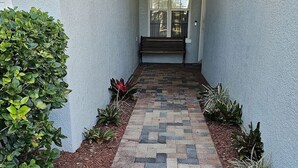 Un chemin pavé mène à un banc et à une porte, de part et d’autre desquels se trouvent des plantes et un paillis.