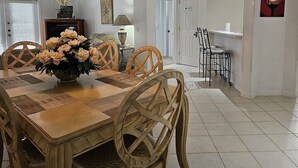 Un coin repas avec une table en bois, des chaises, un vase de fleurs, un luminaire suspendu et une horloge au mur.