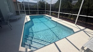 Une piscine à l’eau d’un bleu limpide, entourée d’une clôture blanche, avec en arrière-plan des arbres et un bâtiment.