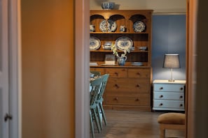 A room with a wooden cabinet displaying blue and white plates, a lamp on a bedside table, and a chair. - Churchill Cottage (Bishop Auckland)