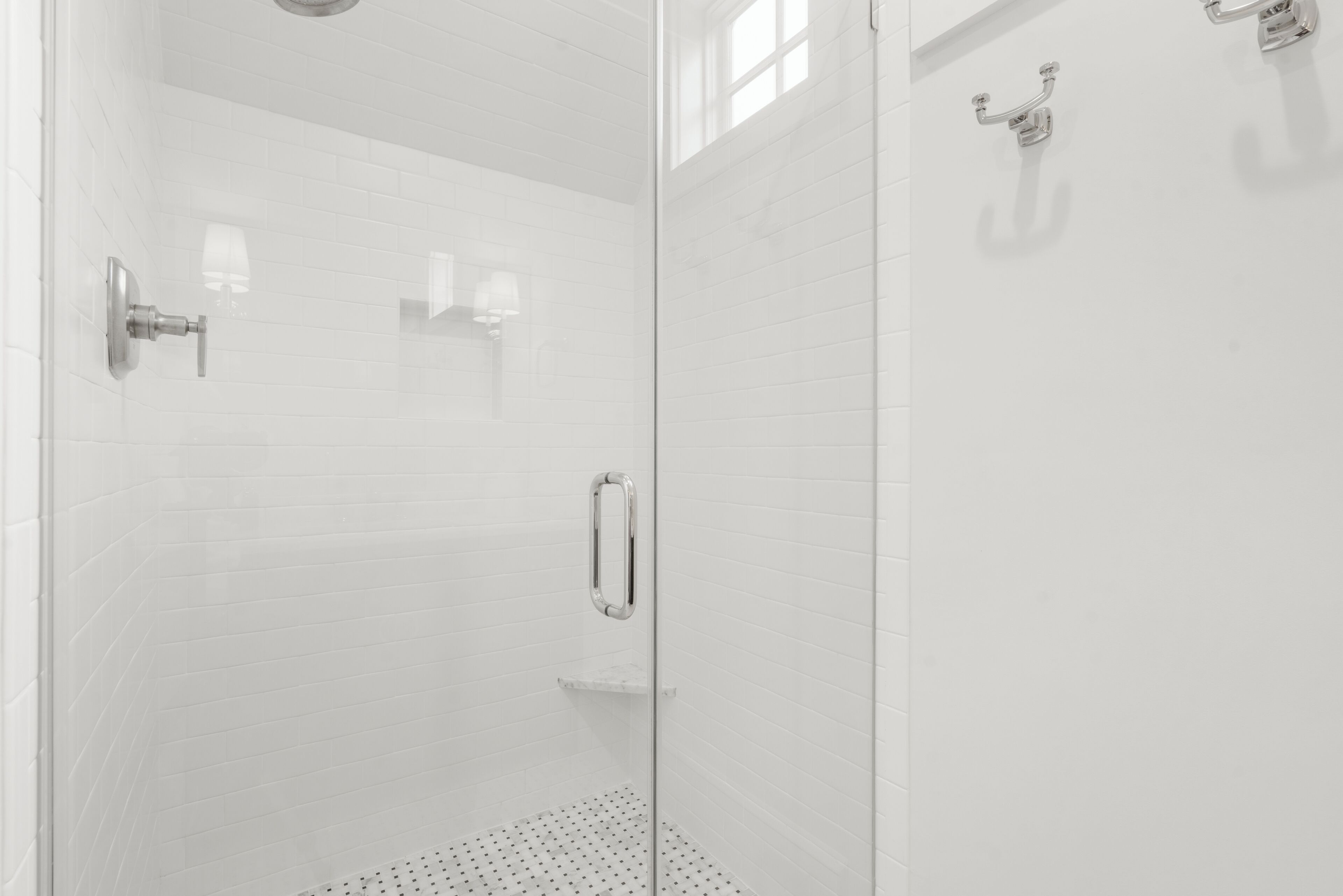A glass-enclosed shower with white tiled walls, a metal faucet, and a shelf.