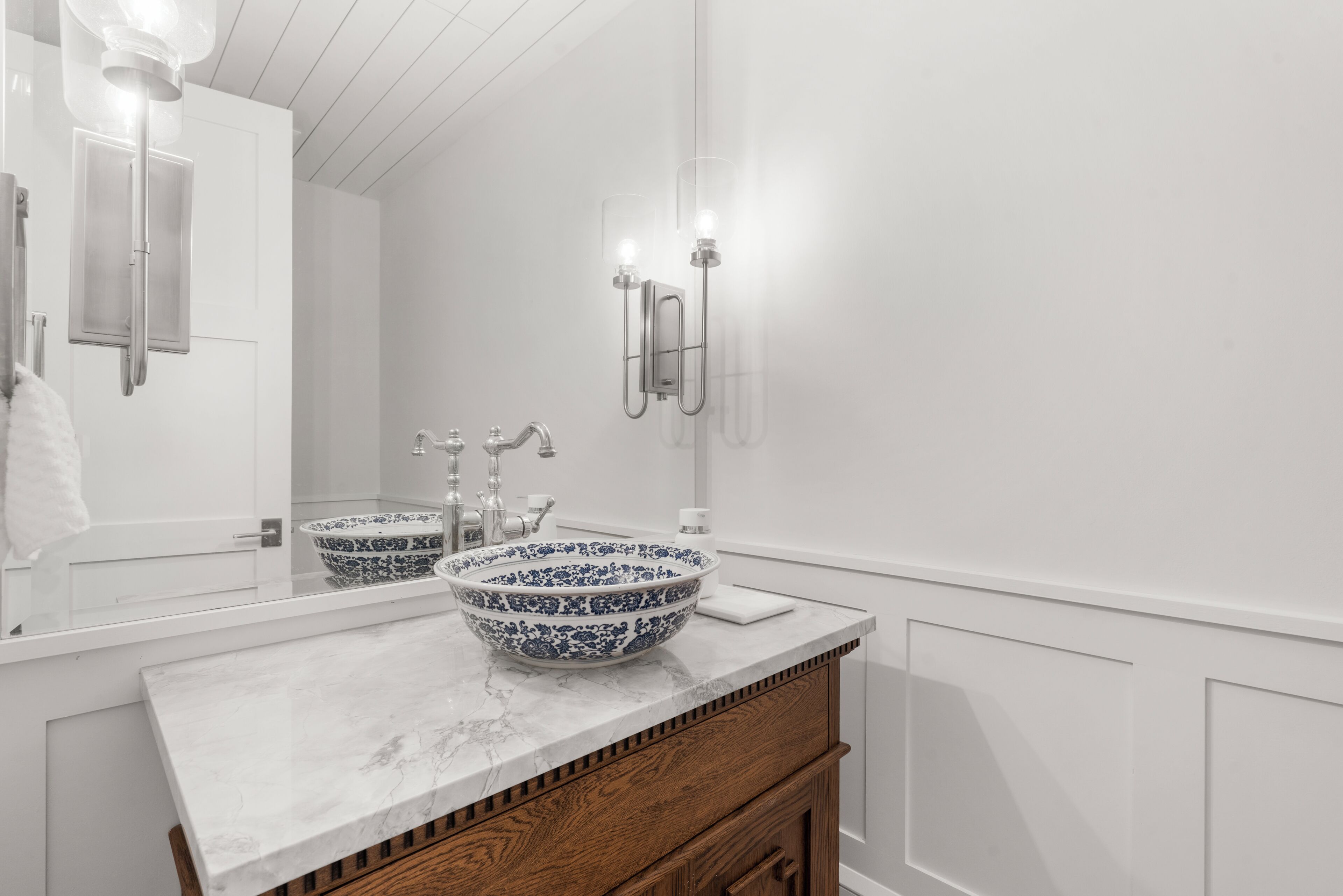 A bathroom with a white vanity, two sinks, a large mirror, and a wall-mounted light fixture.