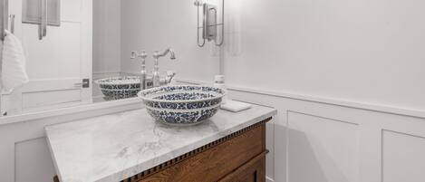 A bathroom with a white vanity, two sinks, a large mirror, and a wall-mounted light fixture.