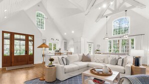 A spacious living room with a large white sectional sofa, a patterned rug, and a kitchen area in the background. - Charming cottage in popular neighborhood (Kiawah Island)