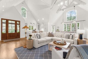 A spacious living room with a large white sectional sofa, a patterned rug, and a kitchen area in the background. - Charming cottage in popular neighborhood (Kiawah Island)