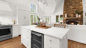 A modern kitchen with white cabinetry, a stone fireplace, and a large island. - Charming cottage in popular neighborhood (Kiawah Island)