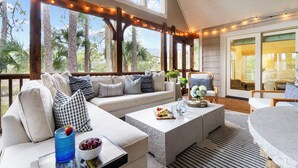 A covered outdoor seating area with a sofa, coffee table, and chairs, overlooking a natural landscape with trees. - Charming cottage in popular neighborhood (Kiawah Island)