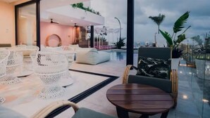 A modern outdoor seating area with wicker chairs, a round wooden table, and a cushioned sofa. - Chic Queen Deluxe Suite in the Heart of PDC (Playa del Carmen)