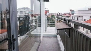 A balcony with a glass door, a view of the cityscape, and a metal railing. - Wake Up to Sunshine in Ninh Binh's Old Quarter - Cozy 2BR for Families! (Hoa Lư)