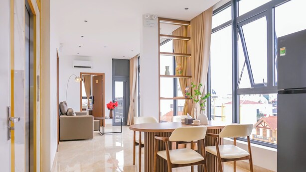 A modern hotel room with a dining area, a sofa, a large window, and a refrigerator. - Wake Up to Sunshine in Ninh Binh's Old Quarter - Cozy 2BR for Families! (Hoa Lư)