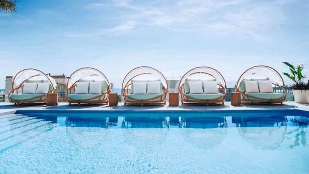 Piscina com seis espreguiçadeiras dispostas em linha.
