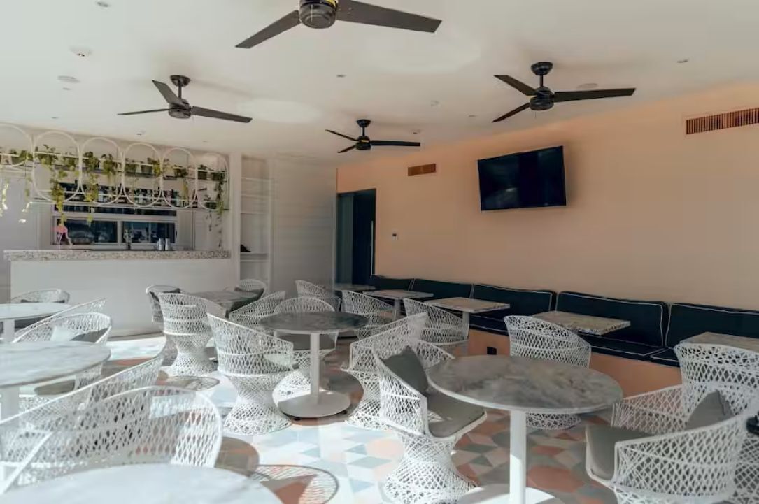 Een restaurant met witte rieten meubels, plafondventilatoren en een televisie aan de muur.