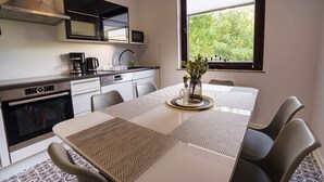A modern kitchen with a dining table, chairs, a coffee maker, and a window with a view of greenery. - ImmoStay-bright apartment with private garden #1 (Bremen)