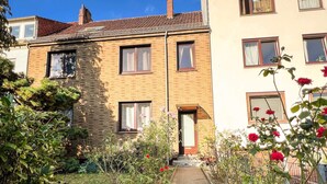 A pathway leading to a residential building with a brick facade and multiple windows. - ImmoStay-bright apartment with private garden #1 (Bremen)