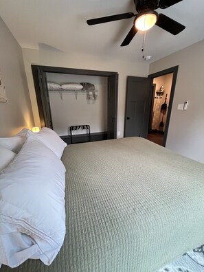 Une chambre à coucher comprenant un lit, un ventilateur de plafond, une armoire et une porte donnant sur une salle de bain.