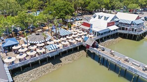 Un muelle con mesas al aire libre y sombrillas, un embarcadero y un edificio de fachada roja y blanca.