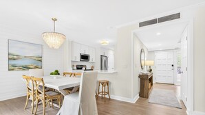 Une cuisine moderne avec des meubles blancs, un coin repas doté d’une table et de chaises blanches, et un lustre.