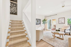 Eine Treppe mit einem gewebten Teppich, ein Wohnzimmer mit einem runden Couchtisch, einem Sofa und einem Fernseher.